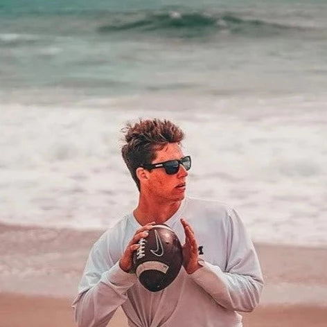 Cade McNamara throws a football on the beach